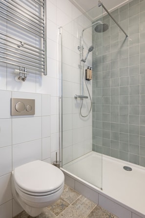 Un baño con ducha de vidrio, inodoro y grifo empotrado en la pared.