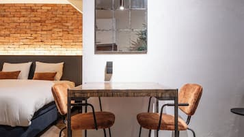 A modern bedroom with a brick wall, a bed with white bedding, a wooden table, two upholstered chairs, and a large mirror.