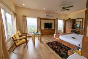 A hotel room with a bed, a desk, a chair, a television, and a ceiling fan.