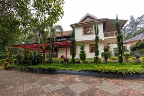 A two-story house with a red roof, surrounded by well-maintained gardens and a paved driveway.