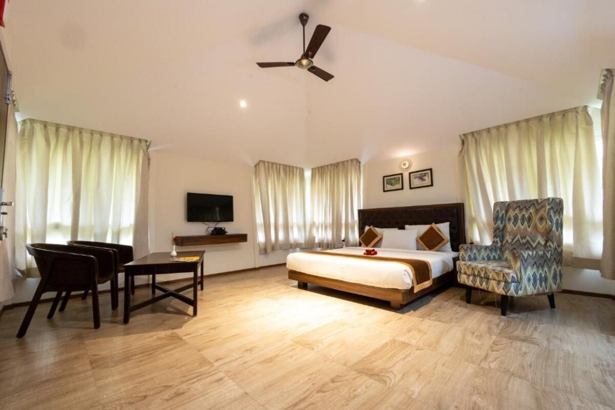 A hotel room with a bed, a desk, a chair, a ceiling fan, and curtains.