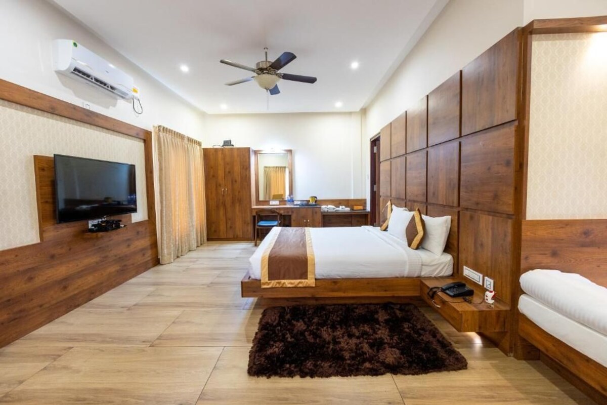 A hotel room with a bed, a television, a ceiling fan, and a wooden wardrobe.