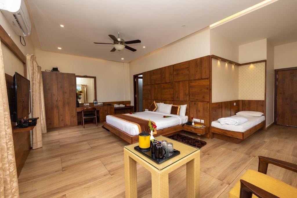 A hotel room with two beds, a small table with a tray, a ceiling fan, and wooden paneling on the walls.