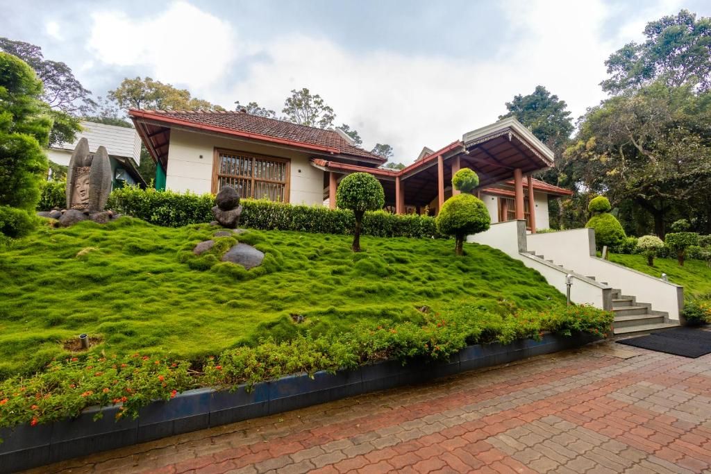 A traditional Japanese-style house with a sloped roof, a stone pathway leading to the entrance, and a well-maintained garden with a variety of plants and a small pond.