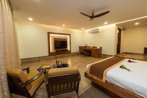 A hotel room with a bed, a desk, a chair, a television, and a ceiling fan.