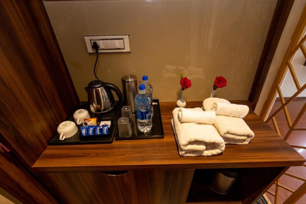 Ein Schreibtisch im Hotelzimmer mit Kaffeemaschine, Wasserflaschen, einer Vase mit einer Rose und Handtüchern.