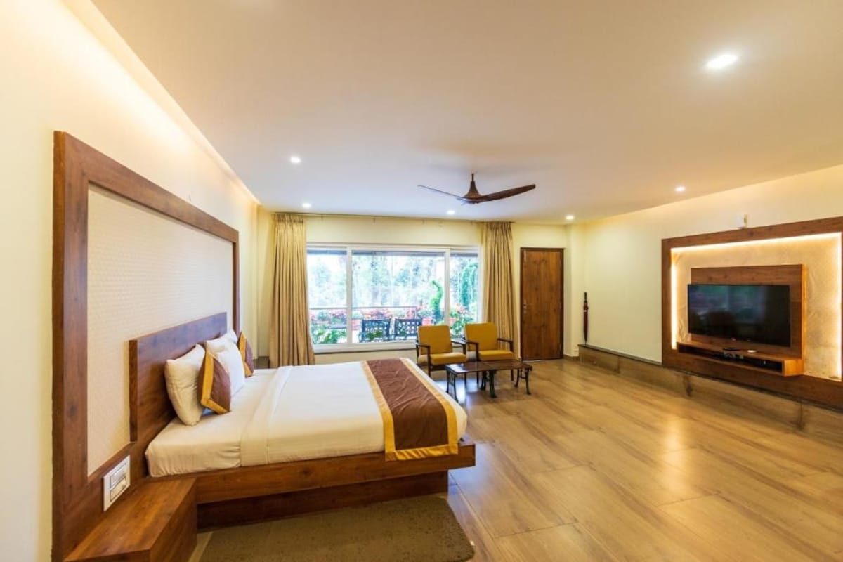 A hotel room with a bed, a television, a ceiling fan, and a view of the outdoors.
