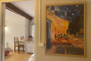 Una habitación con una cama, una silla, una mesa y un cuadro de una escena de café.