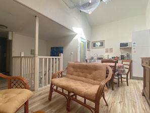Ein Zimmer mit einem Holzstuhl, einem Esstisch mit Stühlen, einer Küchenzeile mit Geräten und einem Balkon mit Geländer.