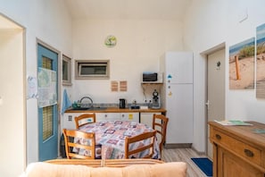 Ein kleines Zimmer mit Küchenzeile, einem Esstisch mit Stühlen, einem Bett und einem kleinen Fenster.