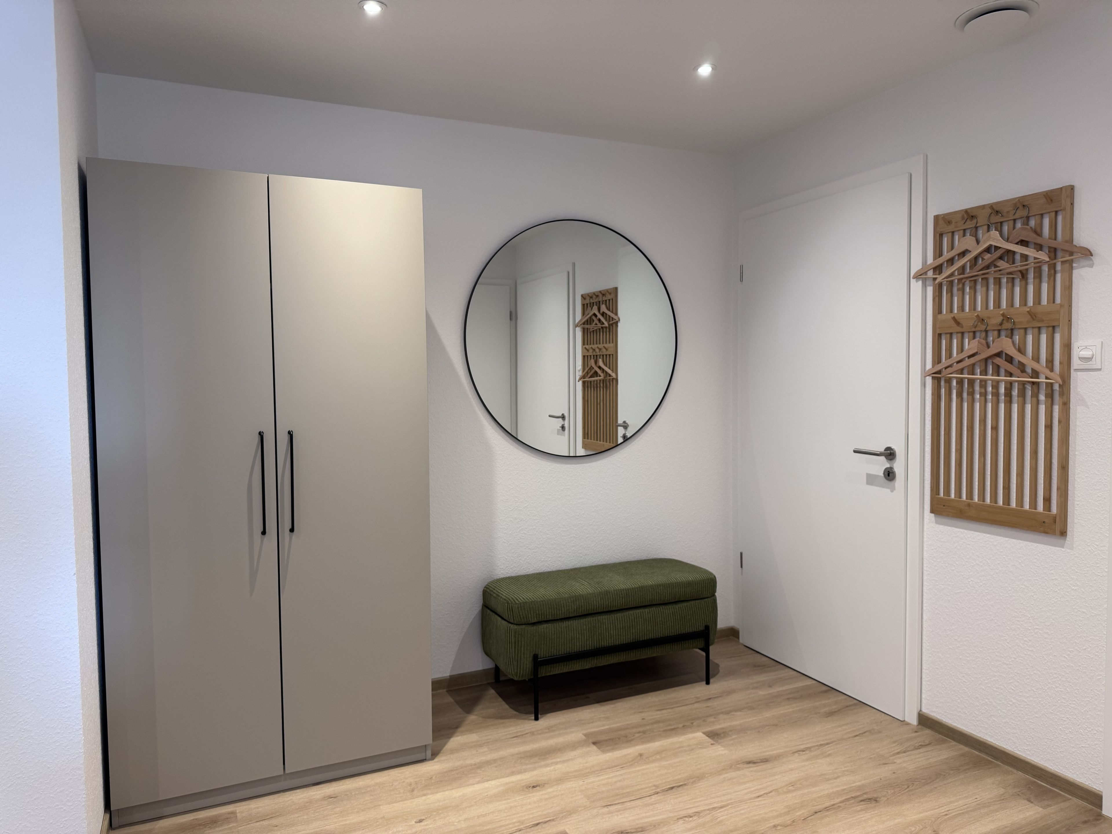 A room with a wardrobe, a bench, a mirror, and a door with a wooden hanger rack.