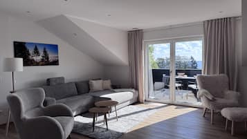 Ein modernes Wohnzimmer mit einer Couch, Sesseln, einem Couchtisch und einem Essbereich mit Tisch und Stühlen.