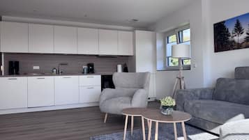 Ett modernt kök med vita skåp, en kaffemaskin och en matplats med en grå soffa och ett litet bord.
