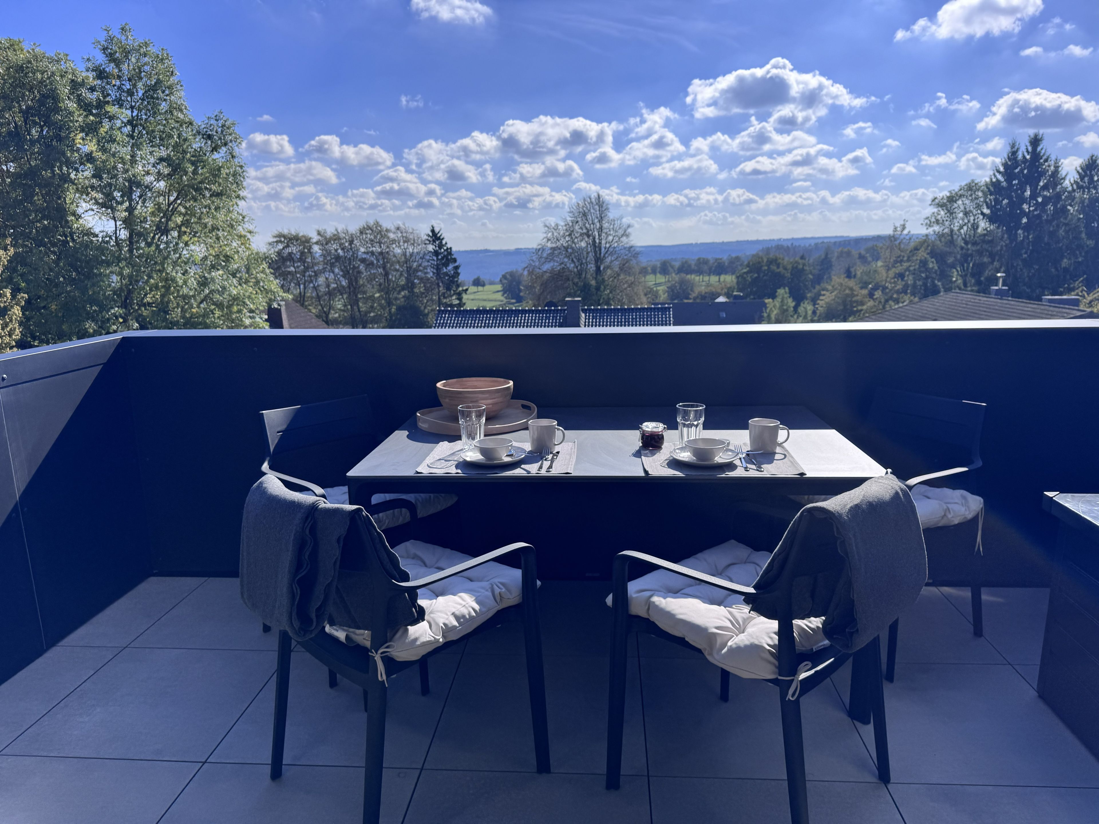 An outdoor dining area with a table set for two, chairs, and a view of the landscape.