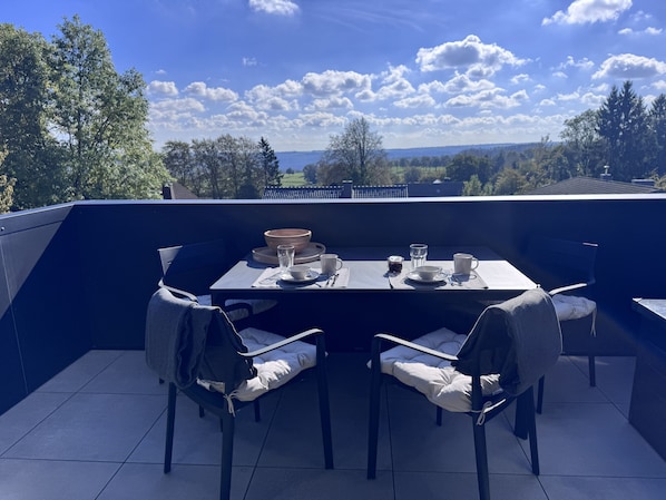 Ein Essbereich im Freien mit einem Tisch für zwei Personen, Stühlen und Blick auf die Landschaft.