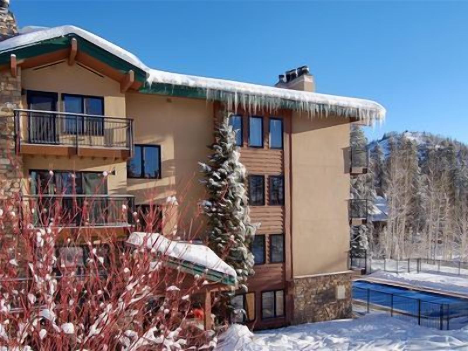 Um edifício de vários andares com varanda no segundo pavimento, piscina e arredores cobertos de neve.