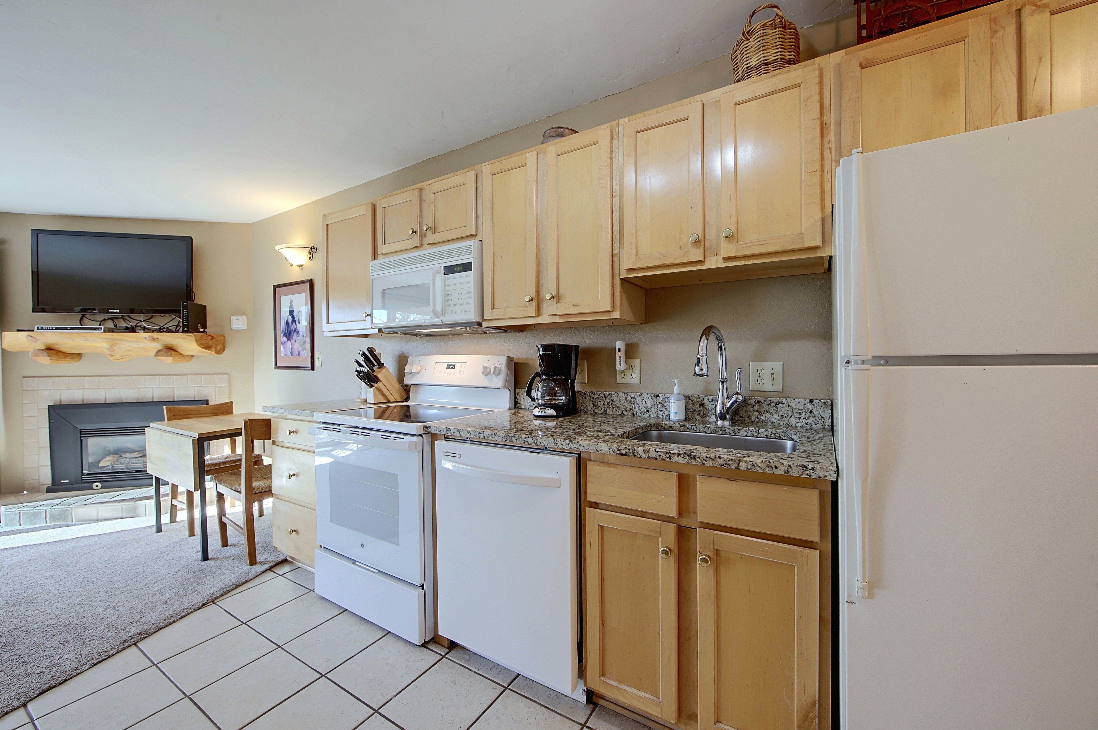 A kitchen with wooden cabinets, a microwave, a stove, a sink, and a television above the fireplace.