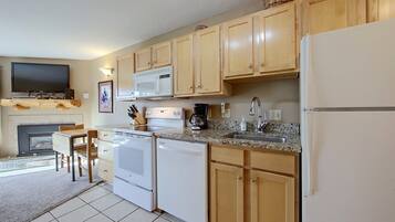 A kitchen with wooden cabinets, a microwave, a stove, a sink, and a television above the fireplace.