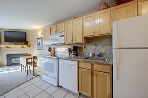 A kitchen with wooden cabinets, a microwave, a stove, a sink, and a television above the fireplace.
