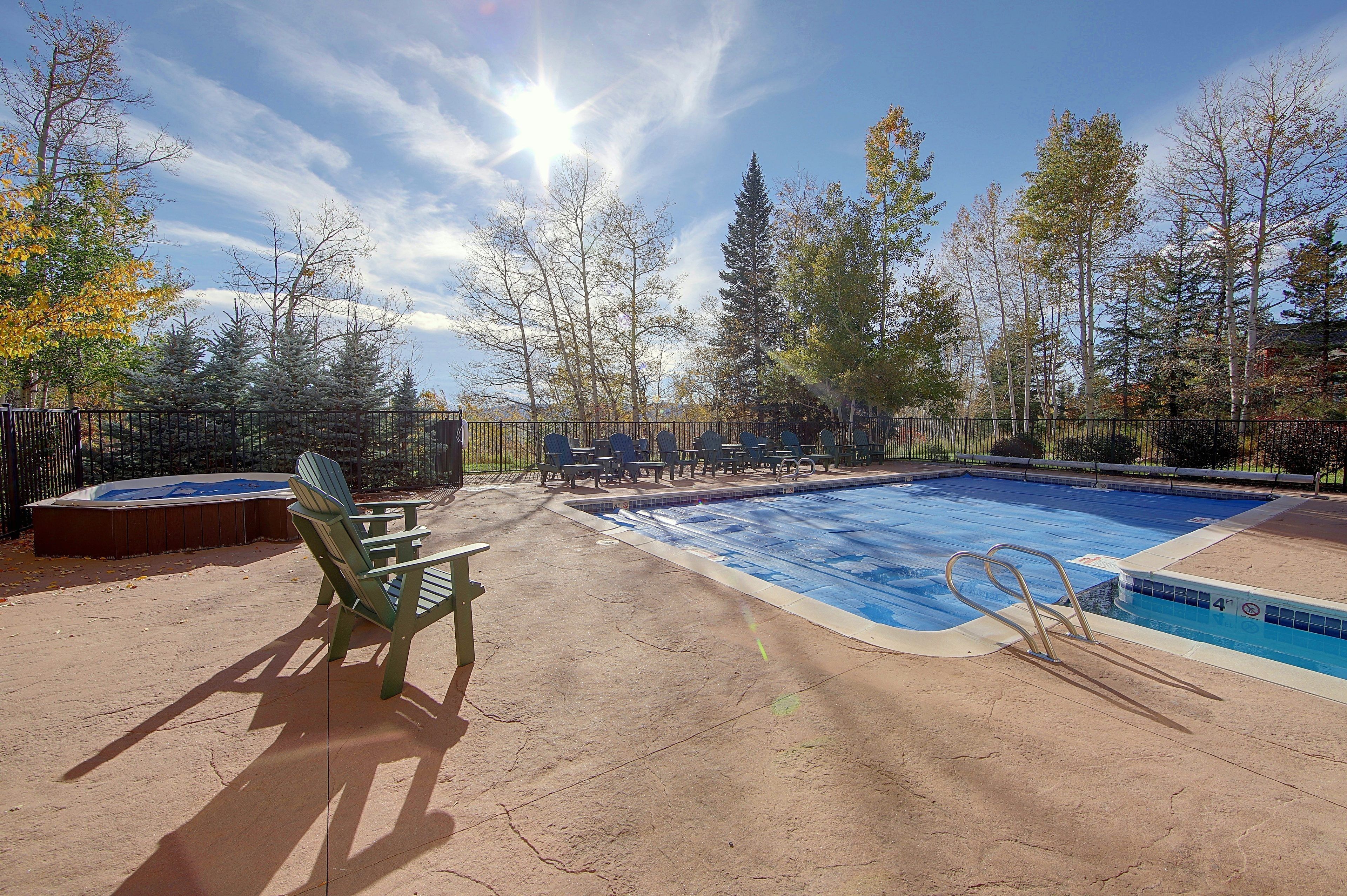 Une piscine avec un jacuzzi, entourée de chaises et de tables, avec des arbres en arrière-plan.