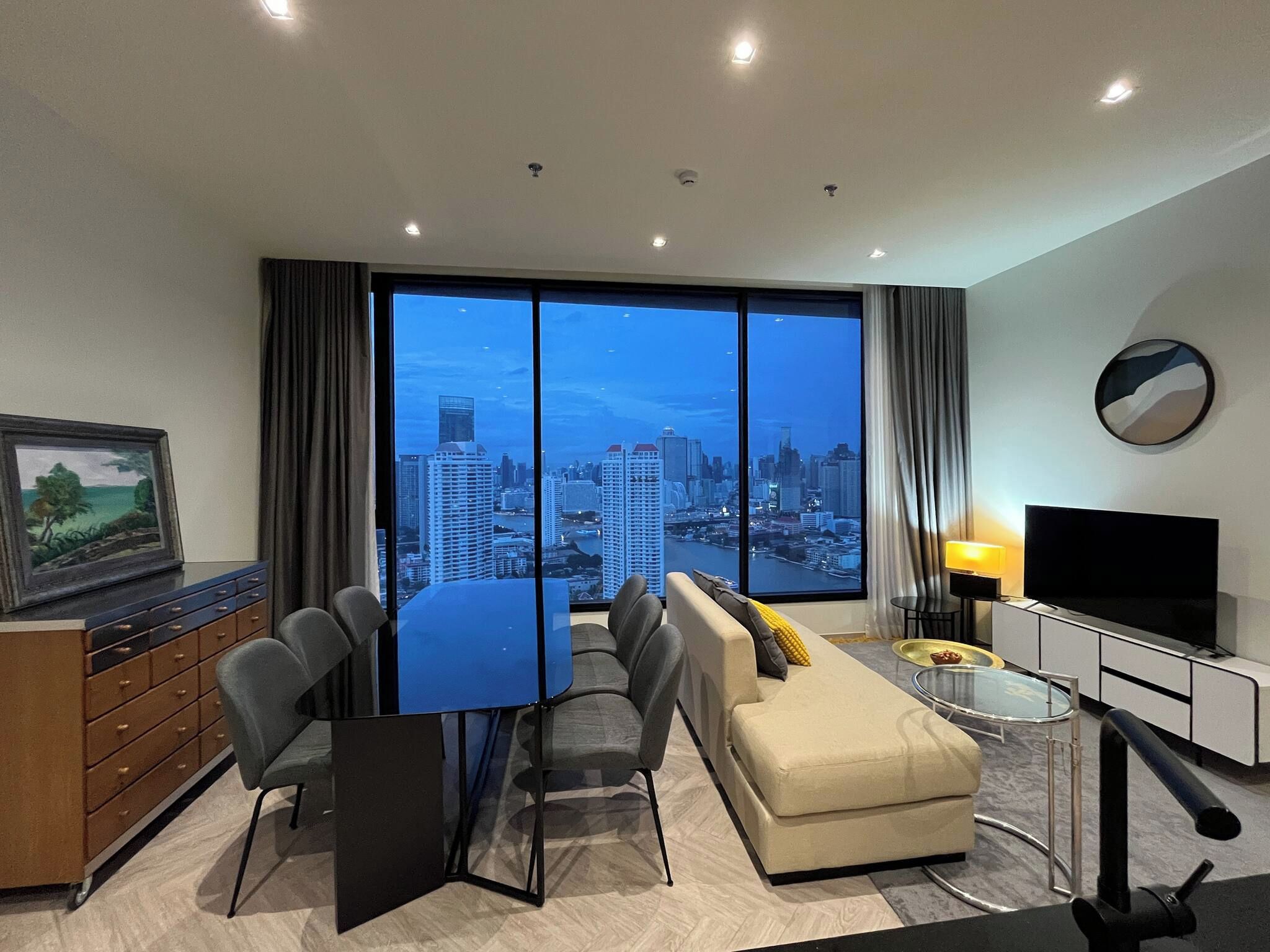 A modern living room with a city view, a dining area, a TV, and a painting on the wall.