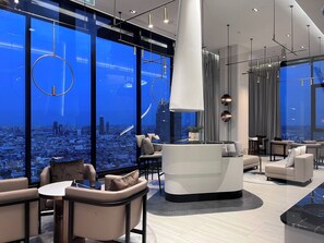 A modern interior with a city view, featuring a reception desk, seating area, and contemporary lighting. - Panoramic River View Condo, Long Stay (Khlong San)