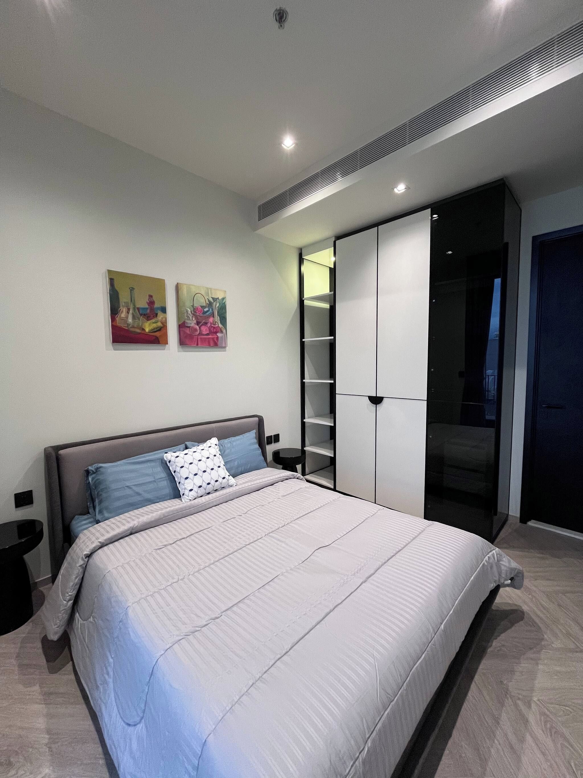 A bedroom with a bed, bedside tables, a wardrobe, and two wall-mounted paintings.