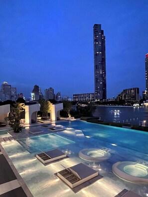 A rooftop pool area with lounge chairs and a view of a city skyline at dusk. - Panoramic River View Condo, Long Stay (Khlong San)