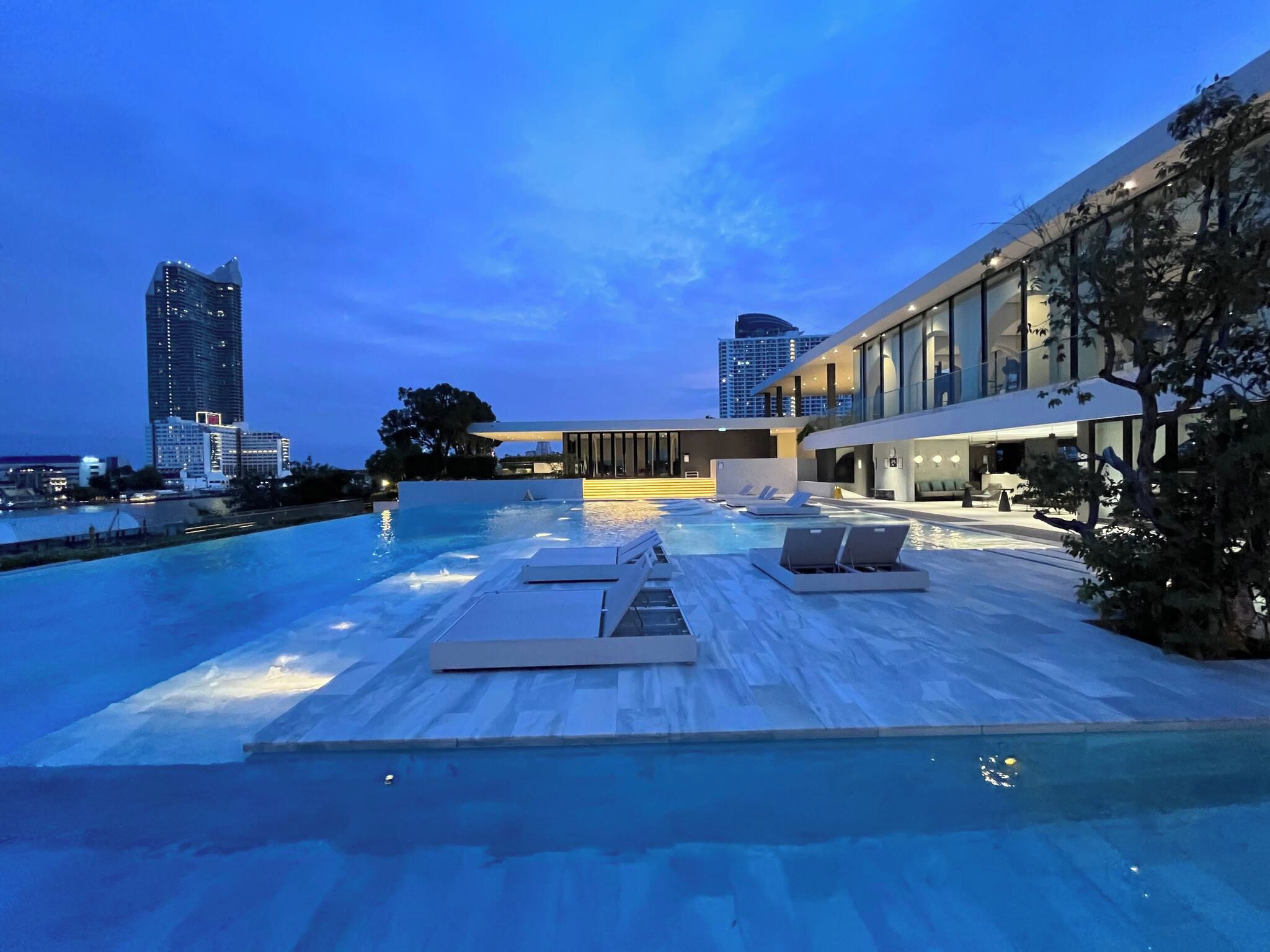 A rooftop infinity pool with lounge chairs and a modern building in the background.