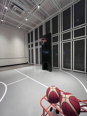 An indoor basketball court with a hoop, two basketballs, and a metal barrier. - Panoramic River View Condo, Long Stay (Khlong San)