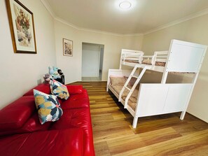 A room with a red sofa, white bunk beds, wooden flooring, and framed pictures on the walls. - Spacious 3BR, 2 Bath, Dbl garage, WIFI, Step-free (Athol Park)