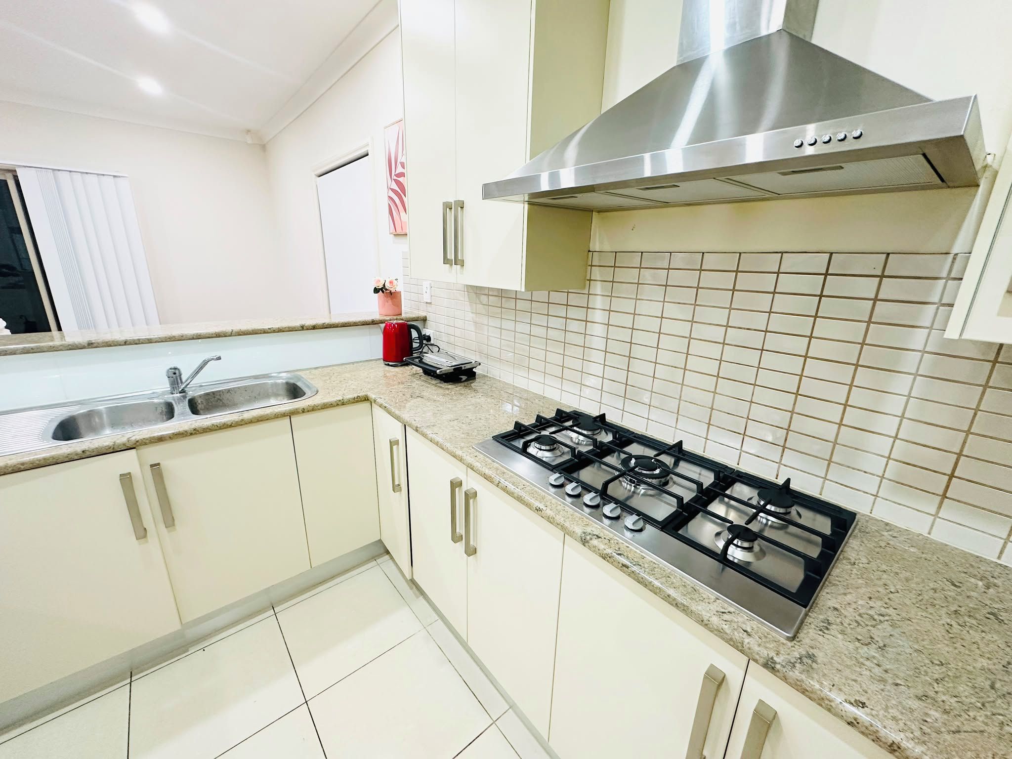 A kitchen with white cabinets, a stainless steel range hood, a gas stove, and a tiled backsplash.