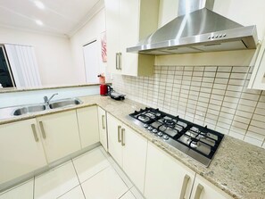 A kitchen with white cabinets, a stainless steel range hood, a gas stove, and a tiled backsplash. - Spacious 3BR, 2 Bath, Dbl garage, WIFI, Step-free (Athol Park)