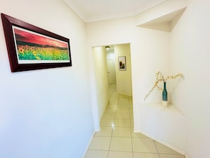 A hallway with a framed painting of sunflowers, a vase with flowers, and a door at the end. - Spacious 3BR, 2 Bath, Dbl garage, WIFI, Step-free (Athol Park)