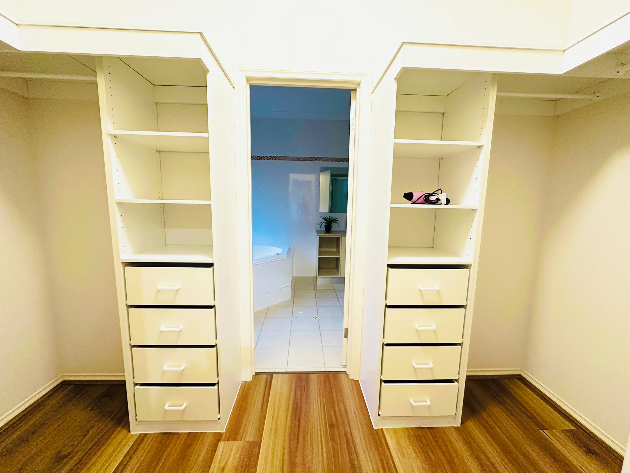 A walk-in closet with open shelving and drawers, leading to a bathroom.