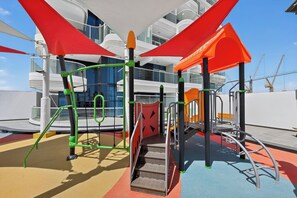 A playground with climbing structures and slides, set against a modern building with balconies. - Bloomfields 1BR in Opalz by Danube (Dubai)
