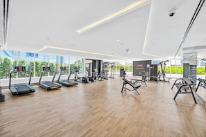 A modern gym with treadmills, weight machines, and a large window offering a view of greenery. - Bloomfields 1BR in Opalz by Danube (Dubai)