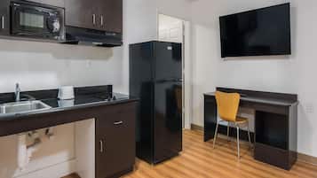 A modern kitchen with a microwave, stove, sink, and black refrigerator. There is a wooden chair and a flat-screen TV mounted on the wall.