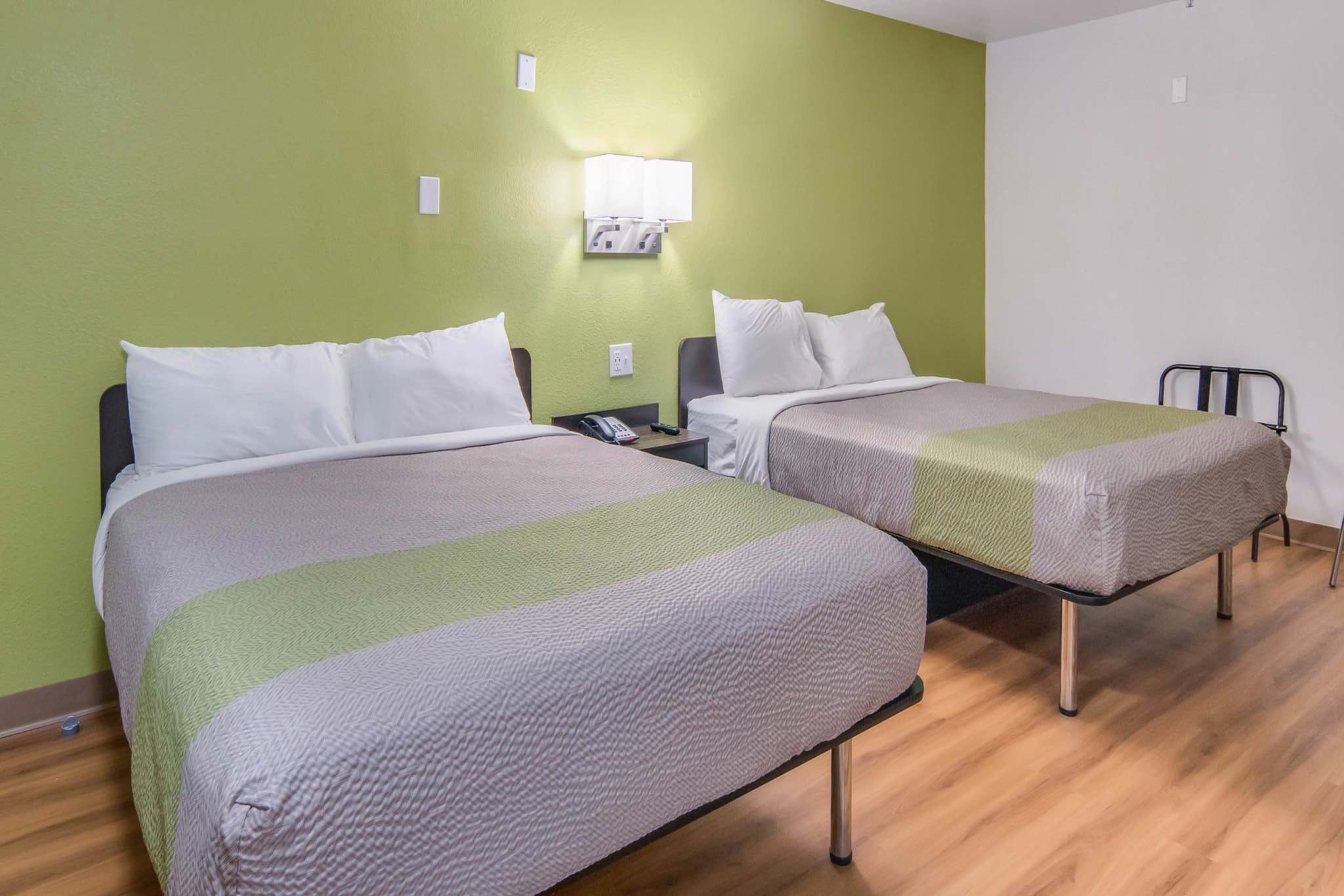 A hotel room with two beds, a bedside table with a phone, and a wall-mounted light fixture.