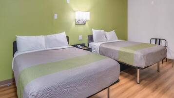 A hotel room with two beds, a bedside table with a phone, and a wall-mounted light fixture.