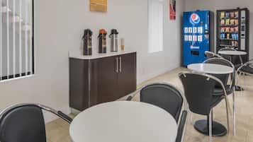 A cafe with round tables and chairs, a vending machine, and a coffee machine on a counter.