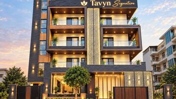 Um edifício moderno de vários andares, com varandas, uma entrada imponente e uma placa com a inscrição 'Tavyn Signature'.