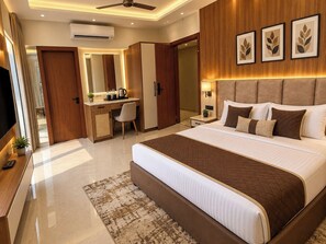 A modern hotel room with a large bed, a desk, a chair, a television, and a ceiling fan. - Tavyn Signature - Noida Sector 117 (Noida)