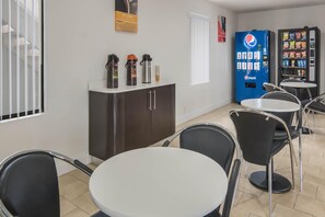 Ein Café mit runden Tischen und Stühlen, einem Automaten und einer Kaffeemaschine an der Theke.