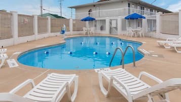 A swimming pool with lounge chairs and umbrellas, surrounded by a white fence with a 'No Diving' sign.