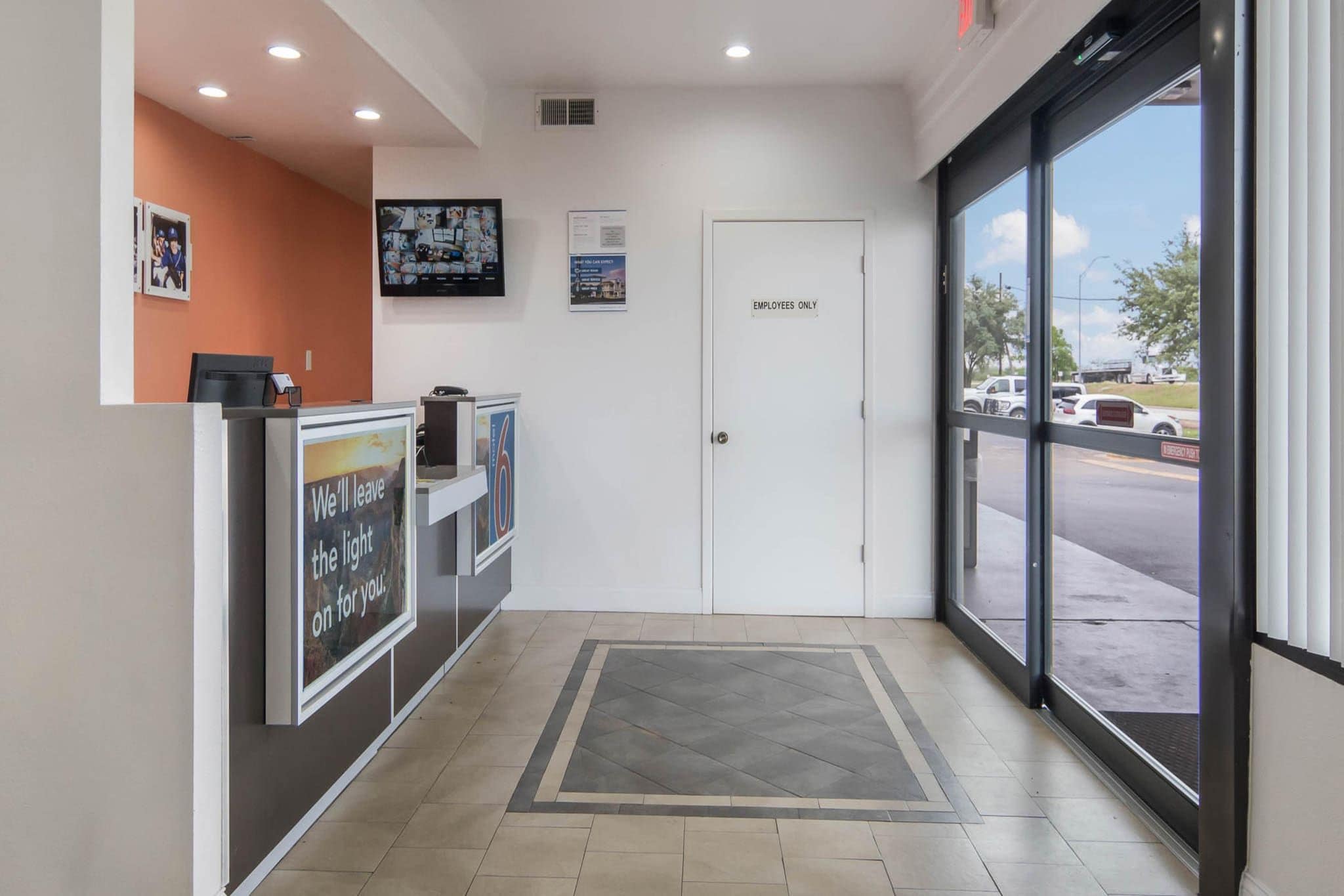 A reception area with a closed door labeled 'EMPLOYEES ONLY,' a counter with a sign saying 'We'll leave the light on for you,' and a television mounted on the wall.