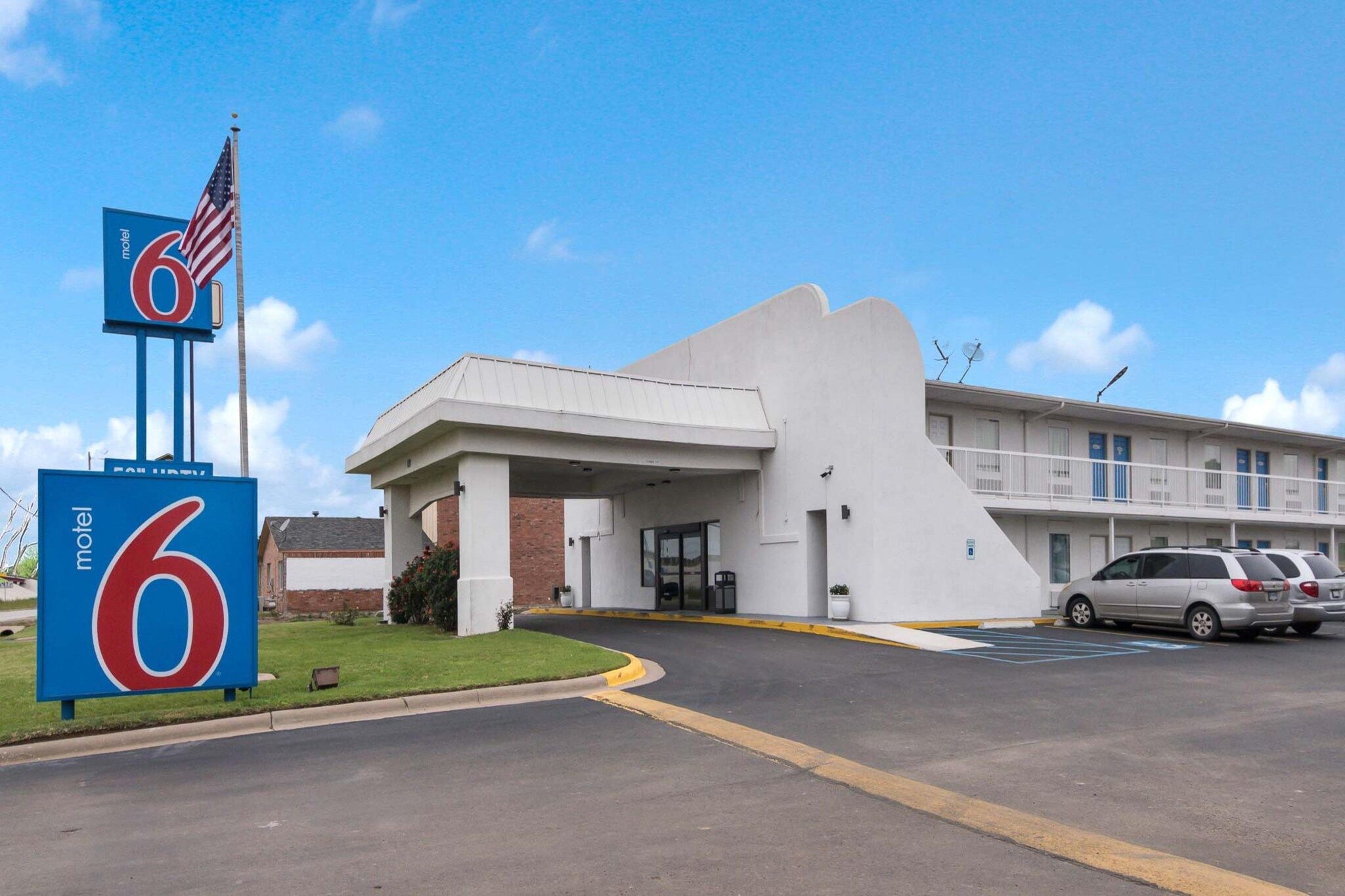 A motel with a large '6' sign, a parking lot, and a building with a flat roof and satellite dishes.