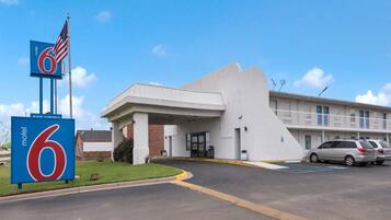 A motel with a large '6' sign, a parking lot, and a building with a flat roof and satellite dishes.