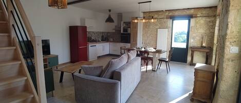 A modern kitchen with a dining area, a sofa, and a staircase.