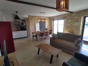 A modern living space with a stone wall, a dining area, a sofa, and a television. - The Charming Sicarderie Guesthouse, 30 minutes from Bordeaux (Peujard)